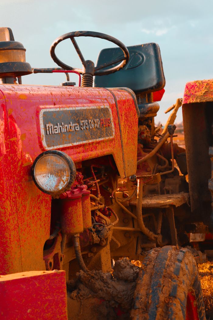 A detailed close-up of a red tractor covered in mud in a rural landscape.