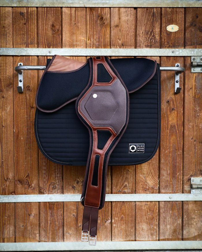 menu-01 Close-up of a horse saddle hanging on a wooden barn wall.