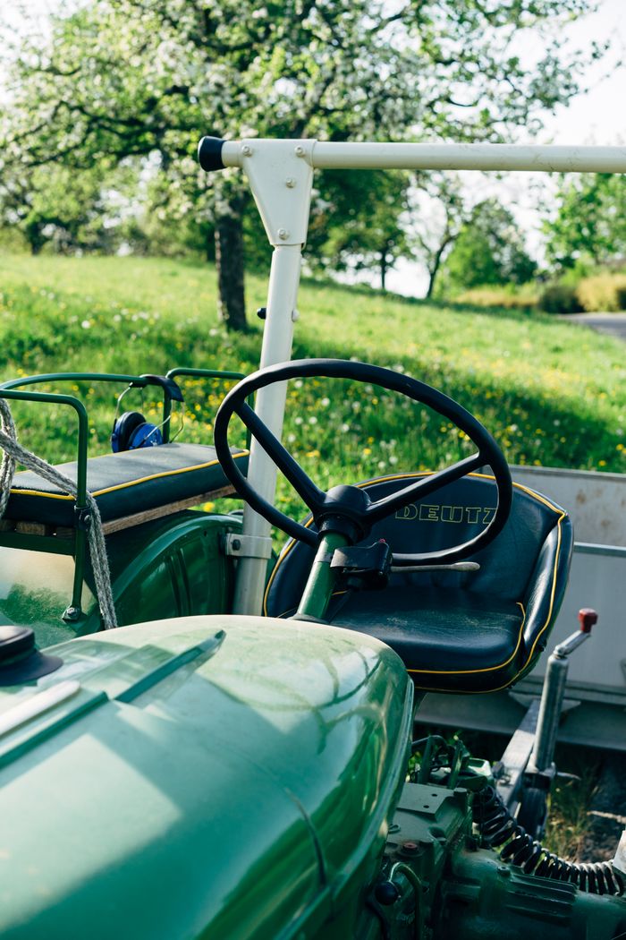 Close-up of a classic green tractor with blooming trees in the background.